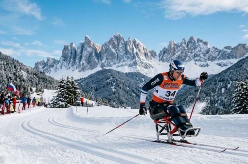 Paralympic cross country skier racing on sit-ski across snowy trail with mountain backdrop