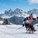 Paralympic cross country skier racing on sit-ski across snowy trail with mountain backdrop