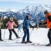 Adult beginner skier in full gear standing at the base of a gentle green run on a sunny day, looking confident and ready to ski for the first time