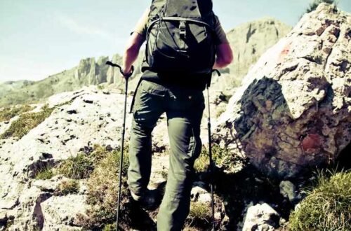 how to use trekking poles for hiking — hiker planting both poles mid-stride on a rocky trail