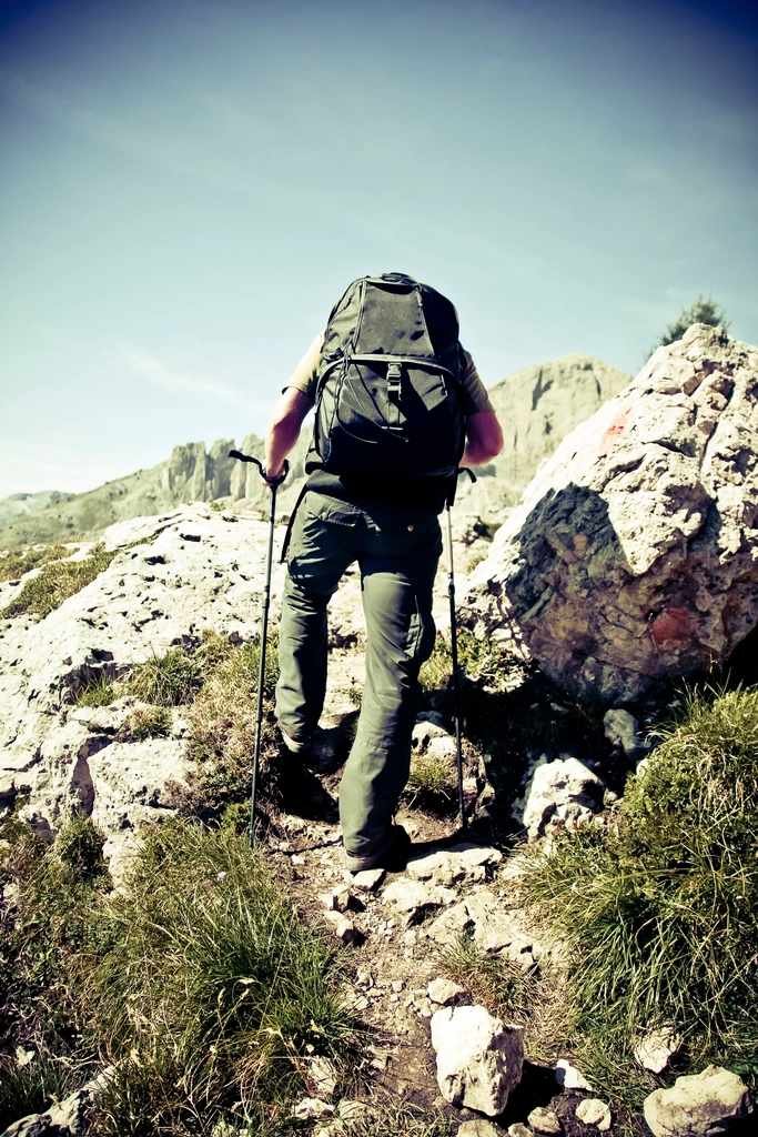 how to use trekking poles for hiking — hiker planting both poles mid-stride on a rocky trail
