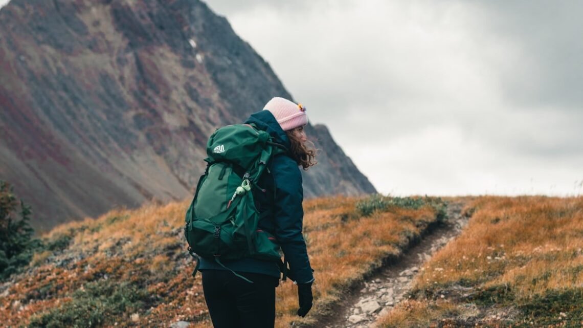 What to wear when hiking: hiker in beanie, shell jacket, leggings, wool socks and boots on a mountain trail