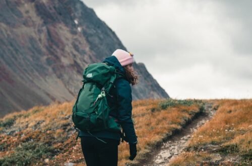 What to wear when hiking: hiker in beanie, shell jacket, leggings, wool socks and boots on a mountain trail