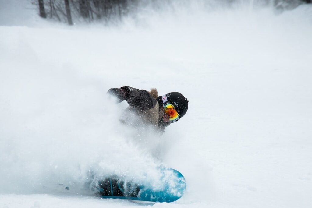 Snowboarder carving deep powder with a hand near the snow, the exact fall pattern wrist guards snowboarding riders wear them for