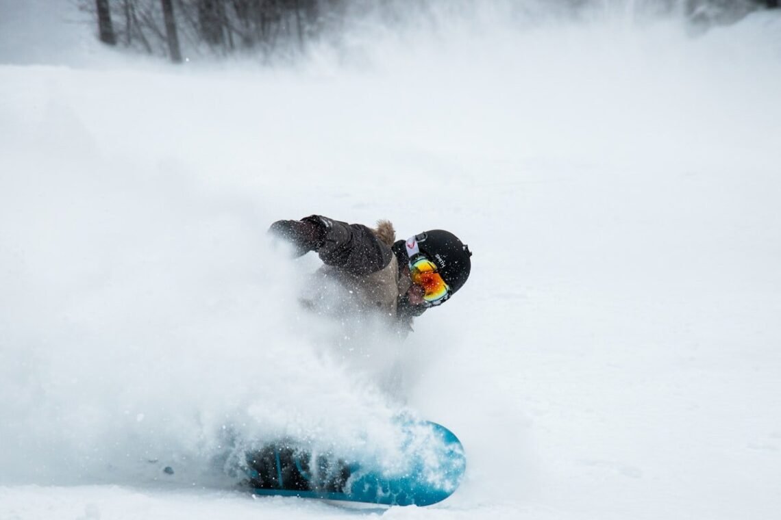 Snowboarder carving deep powder with a hand near the snow, the exact fall pattern wrist guards snowboarding riders wear them for