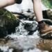 How to prevent blisters while hiking: a hiker in leather boots stepping across wet mossy rocks at a stream crossing