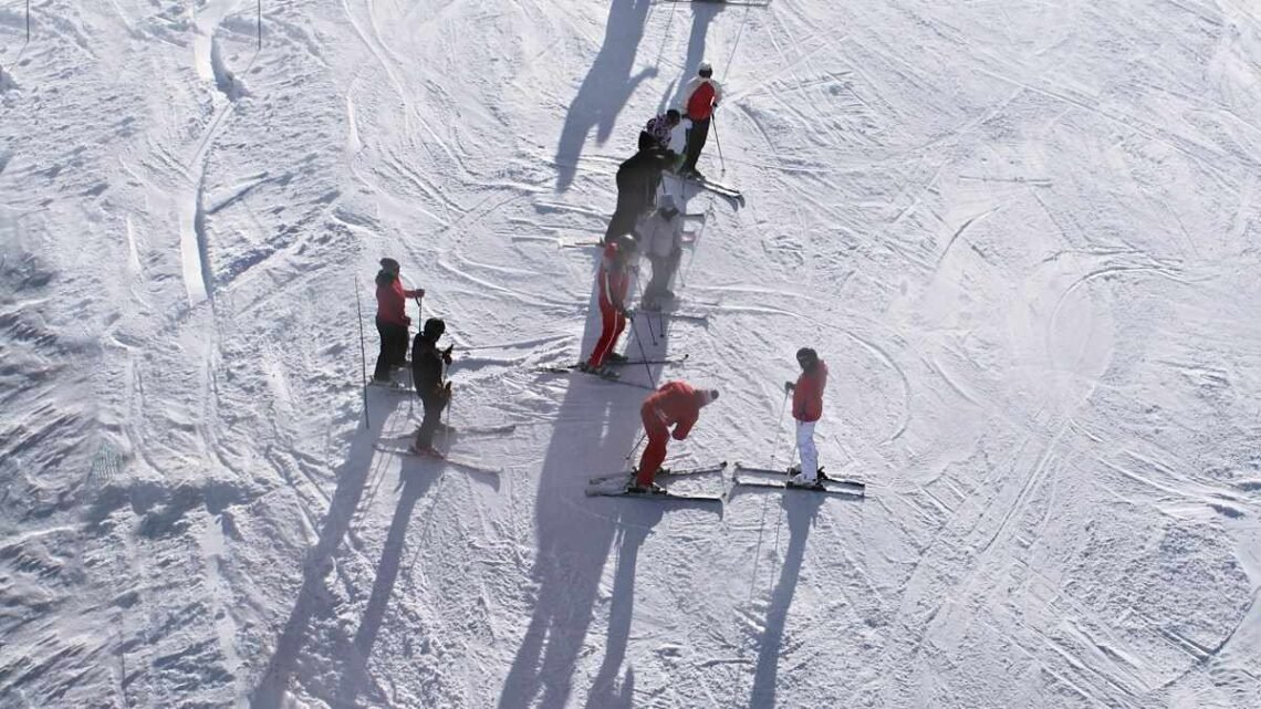 Beginner ski lesson group on a gentle slope deciding skiing vs snowboarding which is easier to learn