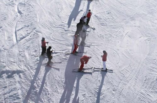 Beginner ski lesson group on a gentle slope deciding skiing vs snowboarding which is easier to learn