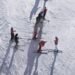 Beginner ski lesson group on a gentle slope deciding skiing vs snowboarding which is easier to learn